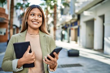 Sokakta akıllı telefon kullanan, kendine güvenen genç Latin bir kadın.