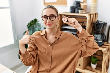 Young blonde woman holding virtual currency bitcoin at the office pointing finger to one self smiling happy and proud 