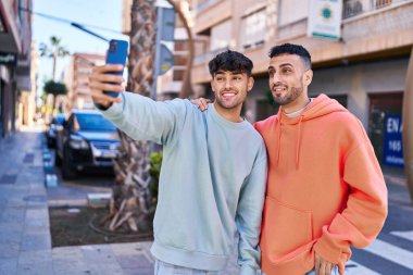 Sokakta akıllı telefondan selfie çeken iki erkek.