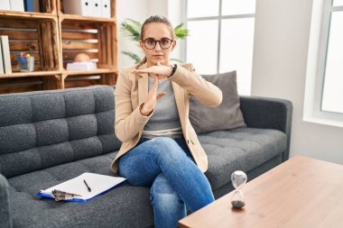 Young woman working at consultation office doing time out gesture with hands, frustrated and serious face 