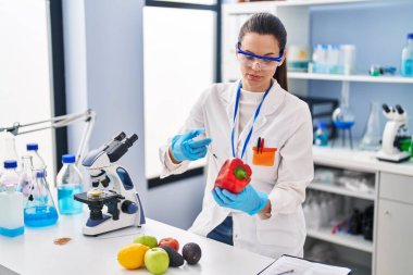 Young beautiful hispanic woman scientist injecting liquid on pepper at laboratory