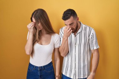 Young couple standing over yellow background tired rubbing nose and eyes feeling fatigue and headache. stress and frustration concept. 