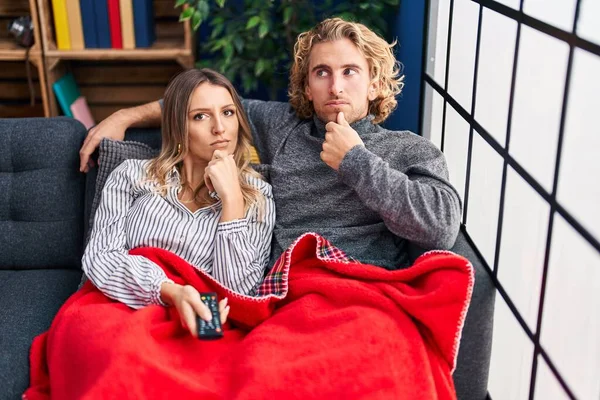 Young Couple Sitting Sofa Home Serious Face Thinking Question Hand — Stock fotografie