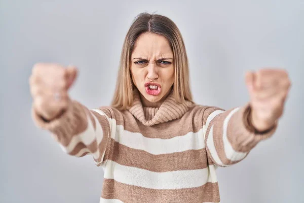 怒りと怒りで叫んでいる間に孤立した背景にタートルネックセーターを身に着けている若いブロンドの女性は怒って拳を上げて激怒しました 怒りと攻撃的な考え方 — ストック写真