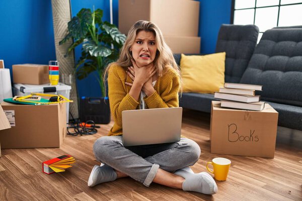 Молодая женщина, сидящая на полу в новом доме, с помощью ноутбука кричит и задыхается, потому что болезненное удушение. проблемы со здоровьем. Концепция асфиксии и самоубийства. 