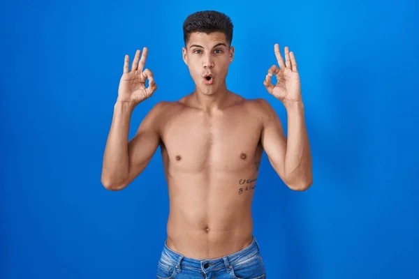 Jonge Spaanse Man Staat Shirtloos Blauwe Achtergrond Kijken Verrast Geschokt — Stockfoto