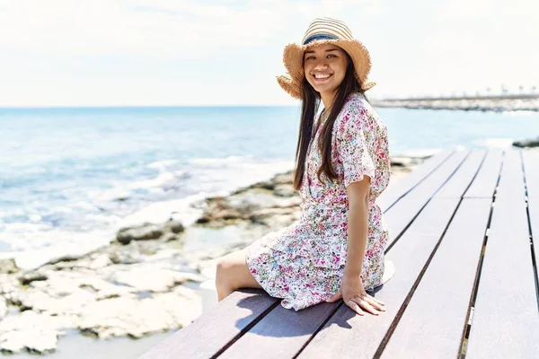 Młoda Latynoska Uśmiechnięta Szczęśliwa Letnim Kapeluszu Siedząca Ławce Plaży — Zdjęcie stockowe