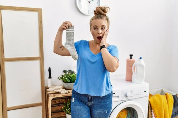 Young Caucasian Woman Holding Dirty Sock Laundry Room Afraid Shocked — ストック写真