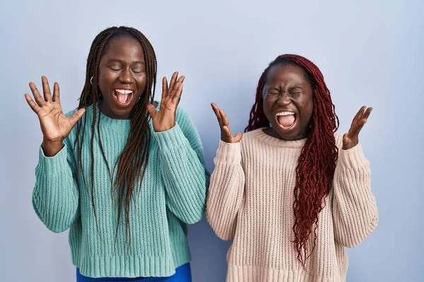 腕を上げて成功のために狂気と狂気を祝う青い背景の上に立っている2人のアフリカの女性は興奮して叫んで目を閉じた 勝者のコンセプト — ストック写真