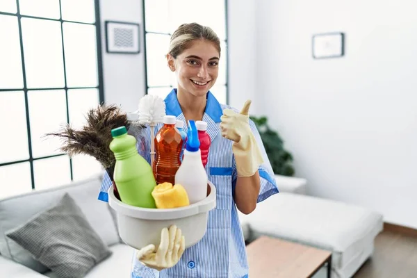 Joven Mujer Rubia Vistiendo Uniforme Limpiador Sosteniendo Productos Limpieza Sonriendo — Foto de Stock