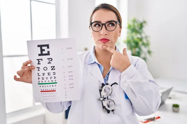 Young Hispanic Optician Woman Holding Medical Exam Serious Face Thinking — Stok fotoğraf
