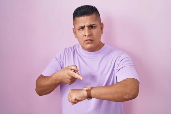 若いですヒスパニック系の男の上に立ってピンクの背景で急いで時間を見るために指す 動揺し 締め切り遅延のために怒っています — ストック写真