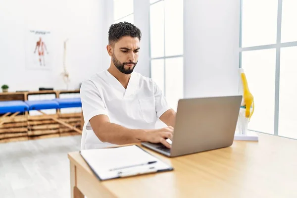 Young Arab Man Wearing Physiotherapist Uniform Using Laptop Clinic — ストック写真