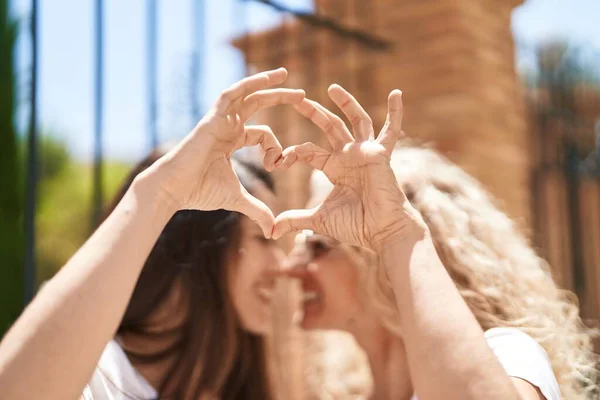 Two women mother and daughter hugging doing heart gesture with hands at street