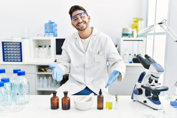 Young hispanic man working at scientist laboratory smiling happy pointing with hand and finger