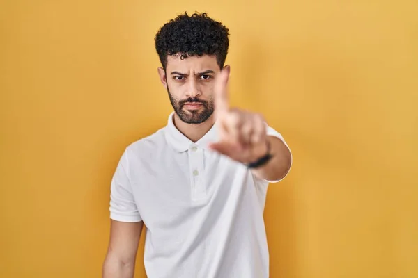 黄色の背景の上に立っているアラブの男は指を上げて怒りの表情で ジェスチャーを示さない — ストック写真