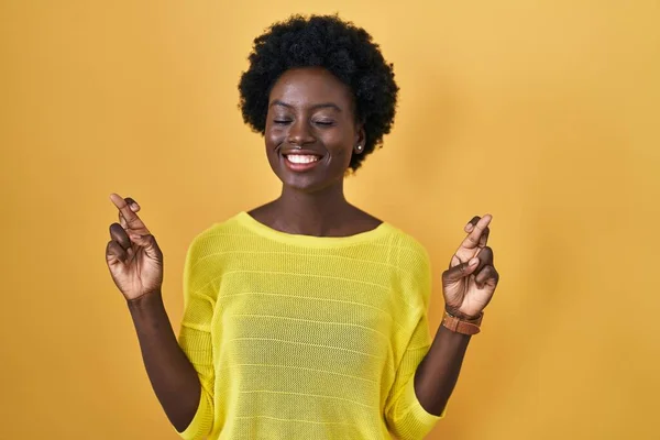 African Young Woman Standing Yellow Studio Gesturing Finger Crossed Smiling — Zdjęcie stockowe