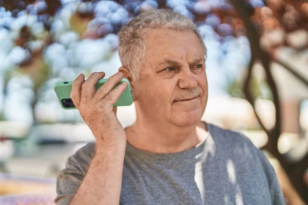 公園で真剣な表情でスマートフォンによる音声メッセージを聞く中年白髪の男 — ストック写真