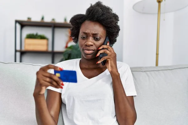 Young african american woman speaking on the phone holding credit card at home