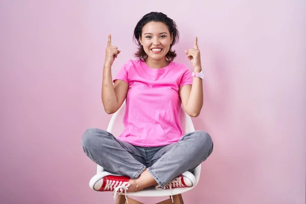 Hispanic Young Woman Sitting Chair Pink Background Smiling Amazed Surprised — 图库照片