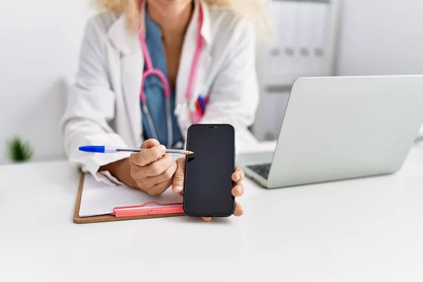 Wanita Pirang Usia Pertengahan Mengenakan Seragam Dokter Menunjukkan Layar Smartphone — Stok Foto