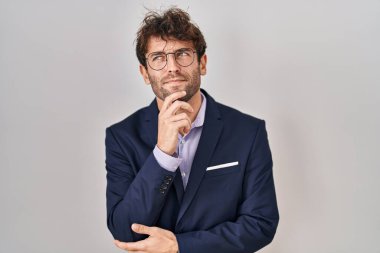 Hispanic business man wearing glasses with hand on chin thinking about question, pensive expression. smiling with thoughtful face. doubt concept. 