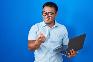 Chinese young man using computer laptop beckoning come here gesture with hand inviting welcoming happy and smiling 