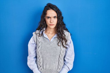 Mavi arka planda duran esmer kadın şüpheci ve gergin, sorun yüzünden surat asıyor. negatif kişi. 