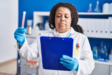 African american woman scientist reading document holding test tube at laboratory