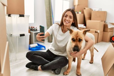 Genç İspanyol kadın kendine güveni tam. Yeni evinde yerde oturan akıllı telefonun yanında selfie çekiyor.