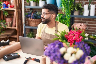 Young arab man florist smiling confident using laptop at florist