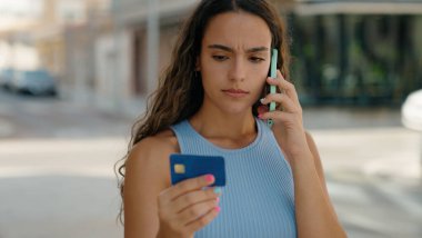 Genç, güzel, İspanyol bir kadın elinde kredi kartıyla akıllı telefondan konuşuyor.