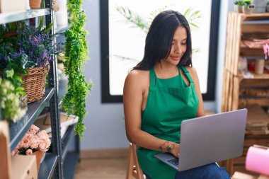 Young hispanic woman florist smiling confident using laptop at florist shop
