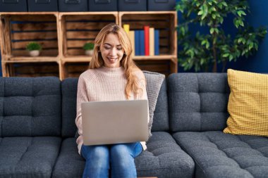 Evdeki kanepede dizüstü bilgisayar kullanan genç bir kadın.