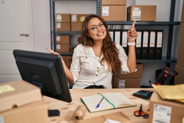 Young hispanic woman working at small business ecommerce smiling confident pointing with fingers to different directions. copy space for advertisement 