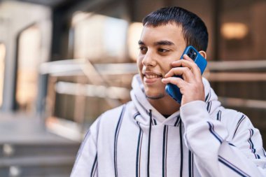 Genç adam gülümsüyor. Kendine güveniyor. Sokakta akıllı telefondan konuşuyor.