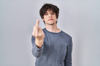 Young man standing over isolated background showing middle finger, impolite and rude fuck off expression 