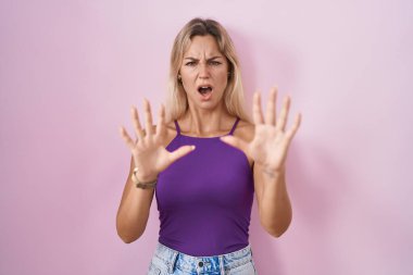 Pembe arka planda duran genç sarışın kadın korku ifadesinden korkmuş ve dehşete düşmüş. El hareketlerini durdur, şok içinde bağır. panik konsepti. 