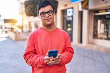 Down sendromlu adam sokakta akıllı telefon kullanarak gülümsüyor.