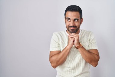 Arka planda sakallı İspanyol bir adam var. Gergin ve heyecanlı bir şekilde çene kenarına bakıyor. 