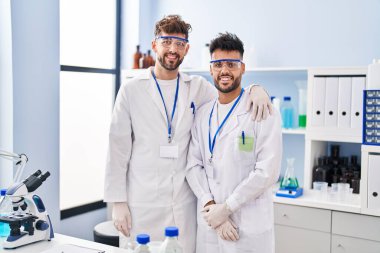 Young couple wearing scientist uniform hugging each other at laboratory