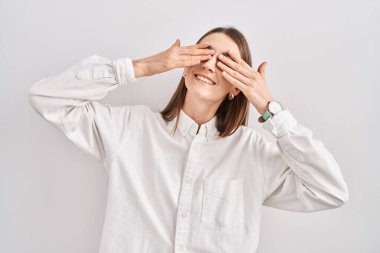 Kafkasyalı genç bir kadın izole edilmiş arka planda duruyor. Gözleri neşeli ve komik gülümseyen ellerle örtüyor. kör kavram. 