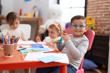 Adorable girl and boy sitting on table cutting paper at kindergarten