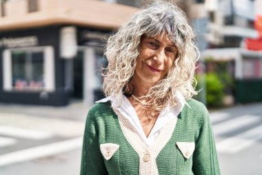 Orta yaşlı bir kadın sokakta kendine güvenerek gülümsüyor.