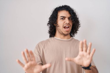 Beyaz arka planda kıvırcık saçlı İspanyol bir adam korku ifadesinden korkuyor ve dehşete düşüyor. El hareketini bırak, şok içinde bağır. panik konsepti. 