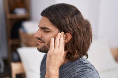 Young hispanic man suffering for headache sitting on bed at bedroom