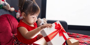 Sevimli Çinli kız evdeki Noel süslemesinin yanında kanepeye oturmuş hediyesini açıyor.