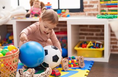 Adorable hispanic girl playing with balls standing at kindergarten