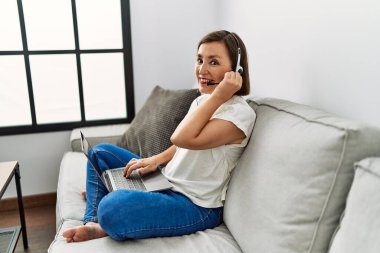 Orta yaşlı İspanyol kadın evde kulaklık takarak kanepede oturuyor.