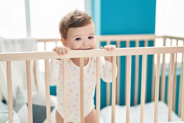 可愛いですCaucasian赤ん坊立っていますオンクレイドルBiting木製Balustradeでベッドルーム — ストック写真